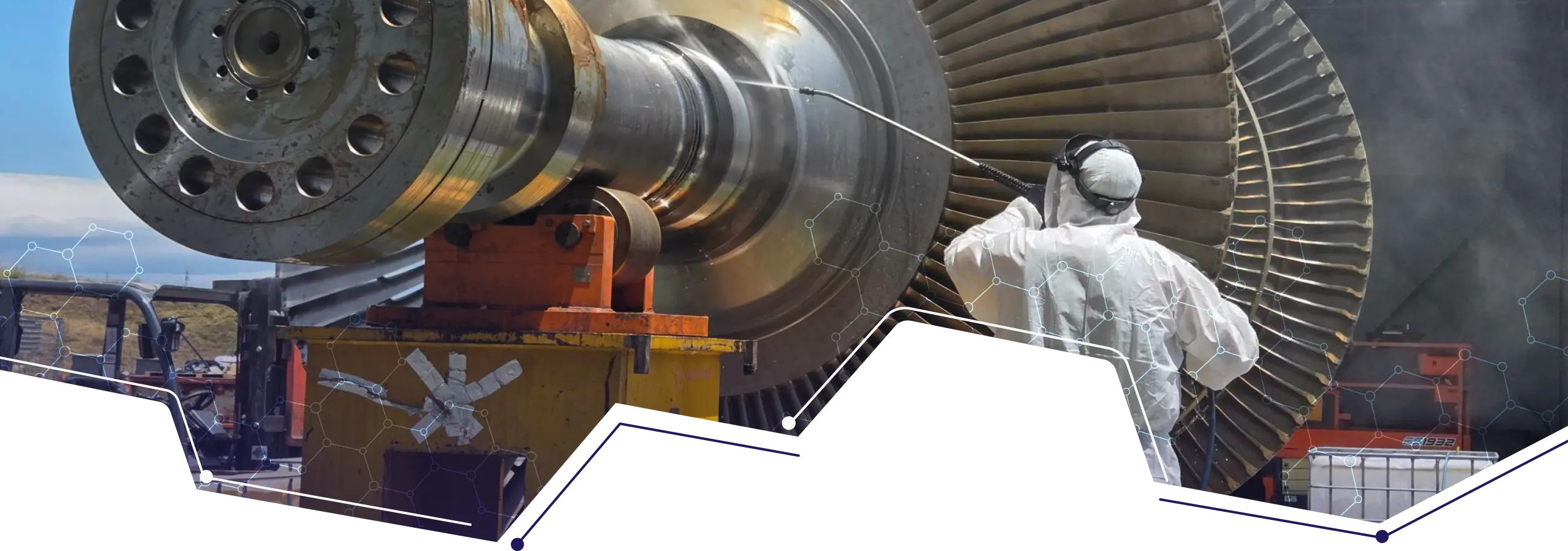 Technician in protective clothing working beside a large industrial turbine rotor and blade assembly