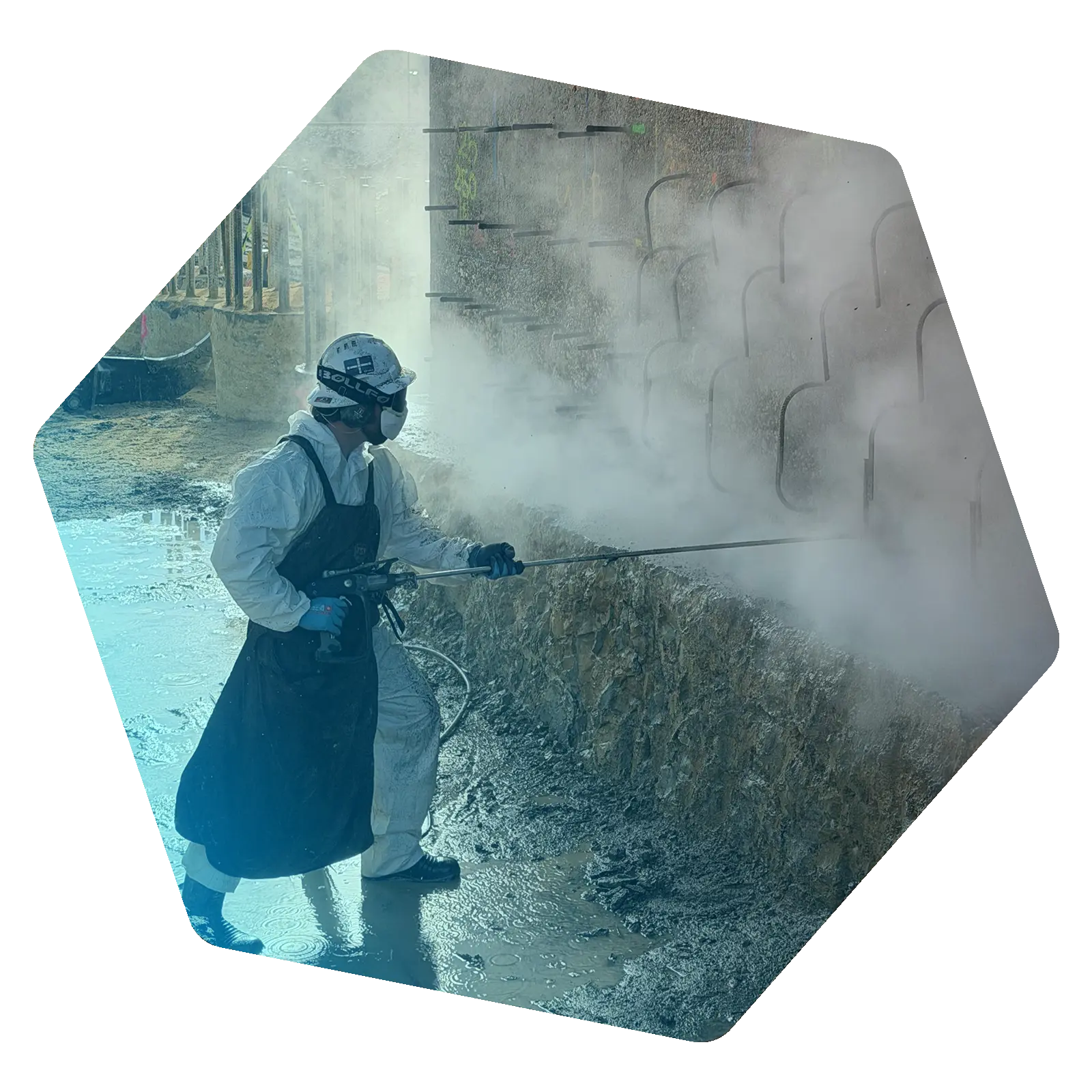 Worker in protective clothing using a water jetting lance against an industrial wall amid heavy spray