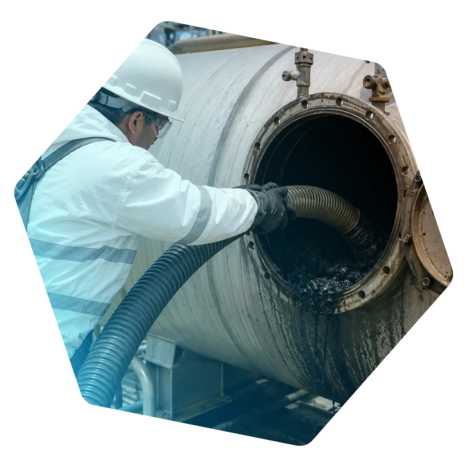 Worker positioning a large hose through the open manway of an industrial tank