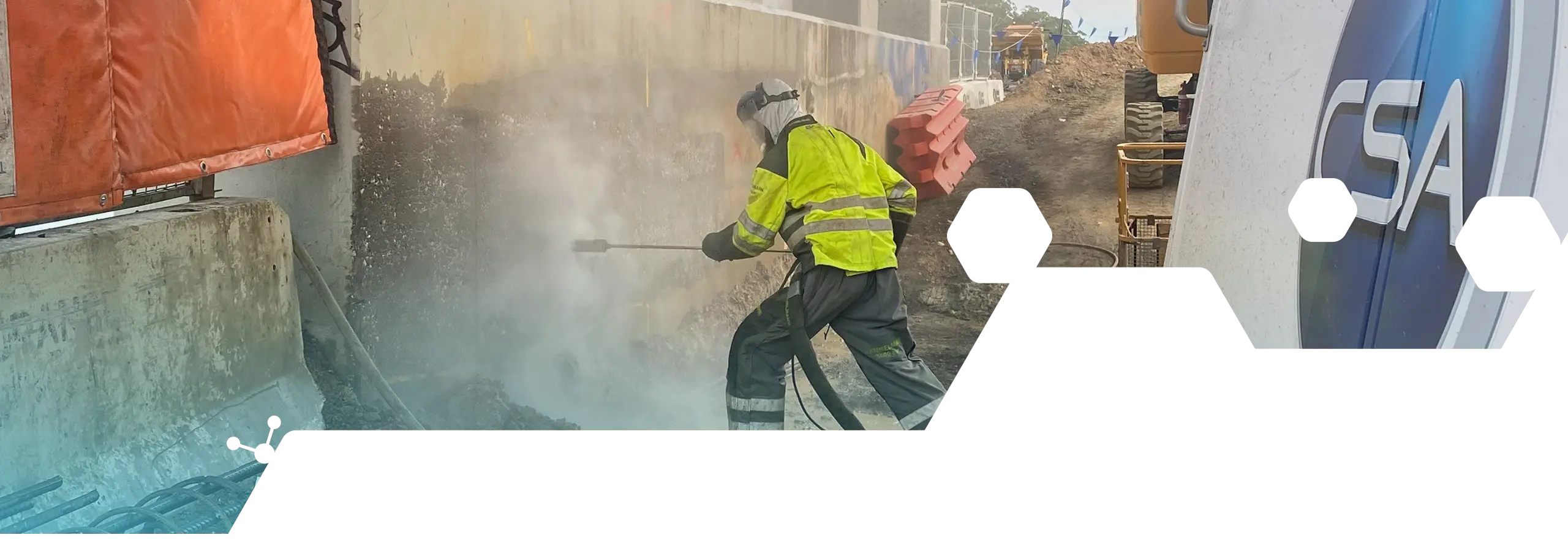 Worker in high-visibility PPE using a water jetting lance on an industrial surface beside CSA service equipment