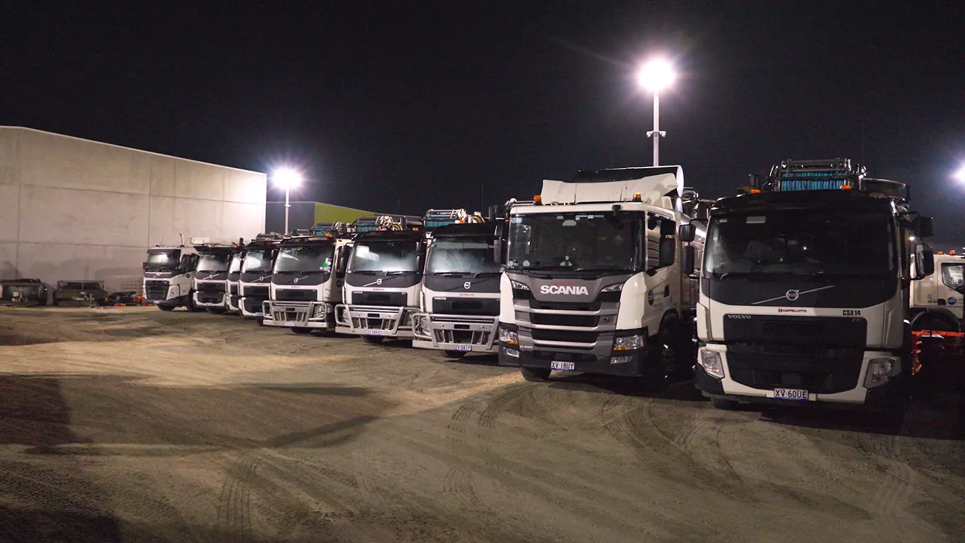 Line of industrial service trucks parked at a depot at night