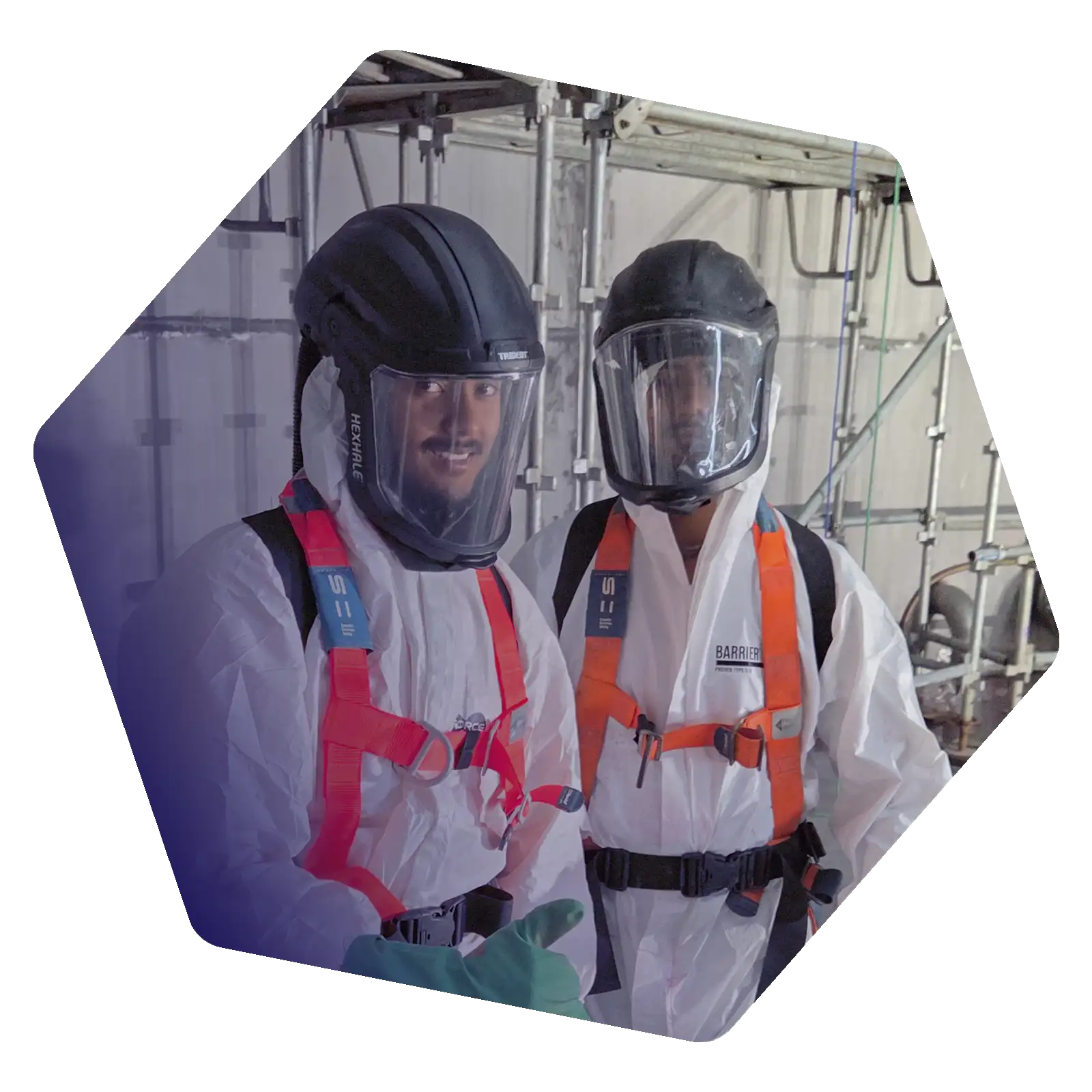 Two industrial technicians wearing protective suits, full-face respirators and safety harnesses inside an industrial facility