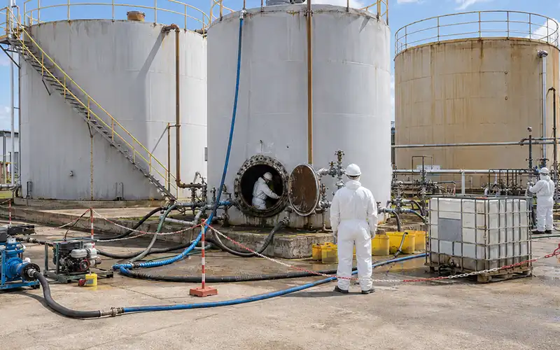 Workers and cleaning equipment positioned beside large industrial storage tanks