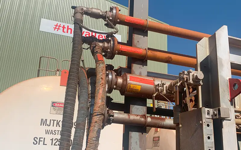 Flexible hoses connected to industrial pipework and valves beside process equipment