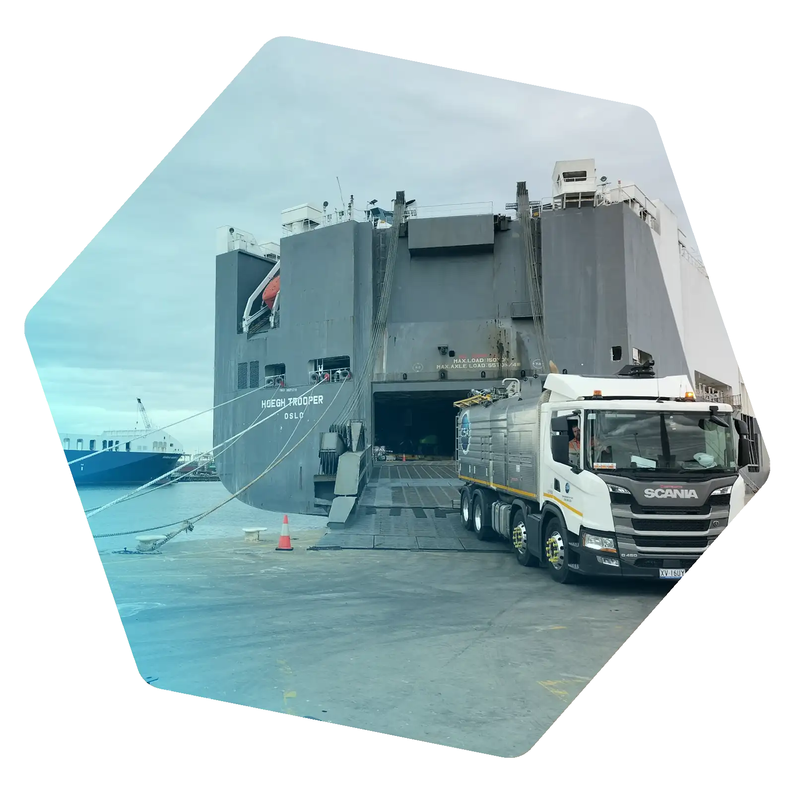 Industrial service truck positioned beside a large vessel at a maritime facility